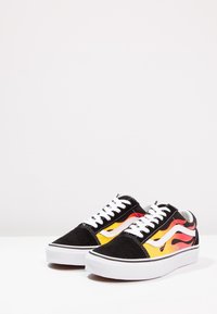 Schwarze Wildledersneaker mit weißen Schnürsenkeln, die ein Flammenmuster in Rot, Orange und Gelb an den Seiten aufweisen. Gummisohle mit schwarzen Akzenten.