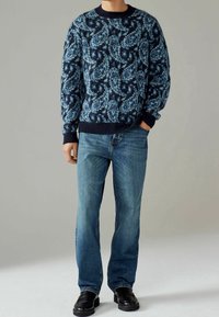 Marineblauer Pullover mit Paisleymuster, langen Ärmeln, gerippten Bündchen und Saum. Getragen mit blauen Jeans und schwarzen Slippern.