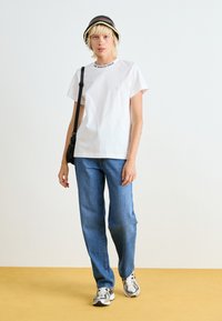 Witte katoenen t-shirt met het "THE NORTH FACE" logo, blauwe spijkerbroek, gestreepte sneakers, en een zwart en crèmekleurige gestreepte bucket hat.