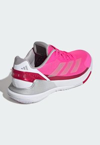 Chaussure de sport rose vif avec une tige en mesh respirant, des accents argentés, un capuchon de talon gris et une semelle blanche texturée avec des détails rouges.
