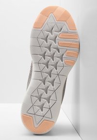 Szara podeszwa trampka z geometrycznym wzorem bieżnika. Charakteryzuje się teksturowaną powierzchnią i pomarańczowym akcentem w pobliżu pięty. Nowoczesny i funkcjonalny design.