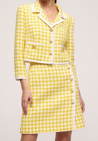 Žlutý tvídový blejzr a sukně se vzorem kohoutí stopy, bílým lemem, zlatými knoflíky a zkráceným sáčkem s dvěma předními kapsami.