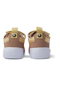 Hnedé a žlté športové topánky s bielymi podrážkami, ktoré majú textúrovaný materiál, remienok na päte a kruhový dizajnový detail na zadnej strane.