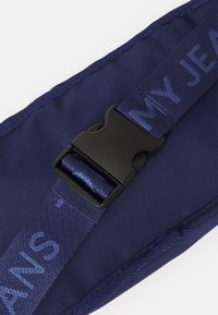 Cinghia in nylon blu con una fibbia in plastica nera; testo "I MIEI JEANS" intrecciato nella cinghia. Texture liscia con dettagli di cucitura lungo il bordo.