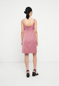 Roze mouwloos jurk met een vierkante achterkant, een getailleerd lijfje en een uitlopende rok, gemaakt van soepele stof. Heeft een rits op de achterkant en minimale naden.