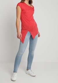 Top corto rojo de manga corta con un dobladillo asimétrico, combinado con unos pantalones vaqueros ajustados azul claro y zapatillas blancas. Textura de tela suave.