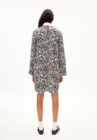 Zwart-wit gestreepte jurk in zebraprint met lange mouwen, een kraag, en een ontspannen pasvorm, gekenmerkt door een textuurstof en een knie-lange snit.