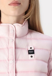 Giacca piumino rosa chiaro con righe orizzontali, colletto alto, bottoni a pressione e un'etichetta nera con la scritta "Blauer: U.S.A."