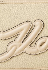 Borsa in pelle texturizzata color crema con un logo in rilievo prominente nella stessa tonalità, bordato in nero e con dettagli di cucitura.