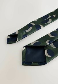 Groene stropdas met een patroon van marineblauwe cirkels en grijze maanen, gemaakt van geweven stof met een gladde textuur en puntige uiteinden.