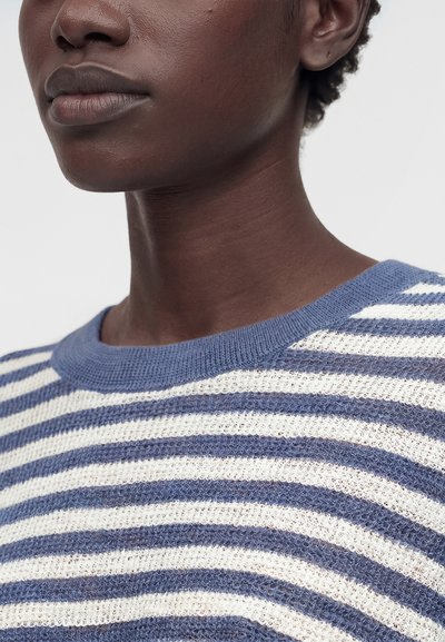 Κοντινό πλάνο του λαιμού και του κάτω μέρους του προσώπου ενός ατόμου που φοράει πλεκτό μπλουζάκι με μπλε και λευκές ρίγες και στρογγυλή λαιμόκοψη.