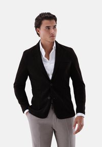 Brauner Samtblazer mit Zwei-Knopf-Verschluss, Revers mit Kerbkragen und Fronttaschen, kombiniert mit einem weißen Hemd mit Kragen.