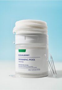 Tarro blanco de almohadillas de tóner con una etiqueta azul. Presenta un acento verde y una tapa transparente. Gotas de líquido residual caen del borde del tarro.