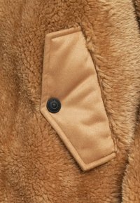 Brun faux fur stof med en stor, glat, gyldent brun plet og en sort knapdetalje. Blød, tekstureret overflade med et hyggeligt udseende.
