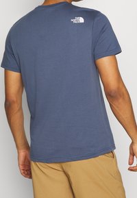 Námořnická modrá bavlněná tričko s krátkými rukávy, s malým bílým logem na zadním rameni. Hladká textura a standardní střih.