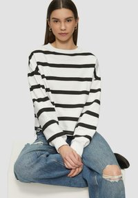 Camicia bianca a maniche lunghe con righe orizzontali nere, caratterizzata da una vestibilità comoda e un collo arrotondato, abbinata a jeans azzurri chiari strappati.