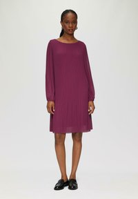 Robe plissée violette à manches longues, décolleté carré et texture subtile ; assortie à des mocassins noirs sur un fond neutre.