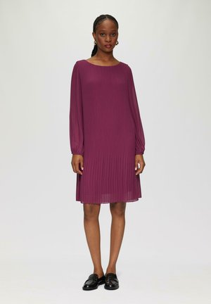 Robe plissée violette à manches longues, décolleté carré et texture subtile ; assortie à des mocassins noirs sur un fond neutre.