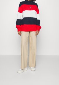 Červeno-bílo-námořnický pruhovaný pletený svetr s vysokým límcem a oversize střihem, doplněný béžovými širokými kalhotami a bílými teniskami.