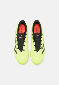 Zapatillas de fútbol verde lima con cordones y acentos negros, que presentan una superficie texturizada y un forro interior negro acolchado.