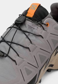 Helle graue Schuhe mit strukturiertem Finish, schwarzen Akzenten und einem orangefarbenen Zugverschluss. Verfügt über einen gepolsterten Kragen und flexible Schnürsenkel für einen sicheren Sitz.