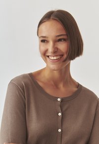 Bruine gebreide cardigan met een ronde hals, voorzien van vijf witte knopen aan de voorkant en korte mouwen. Gladde textuur en getailleerd ontwerp.