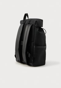 Juodas kuprinės, pagamintos iš tekstūruoto audinio, su ritinio viršumi, patogiai reguliuojamais paminkštintais diržais ir šoniniu kišeniu. Pabrėžia elegantiškus, minimalistinius akcentus.