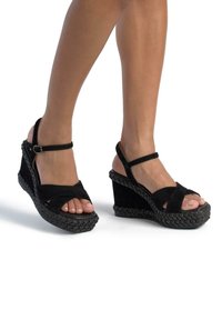Schwarze Wildleder Wedge-Sandalen verfügen über eine geflochtene Sohle, ein offenes Zehen-Design und einen verstellbaren Knöchelriemen. Der Wedge-Absatz sorgt für Höhe und Unterstützung.