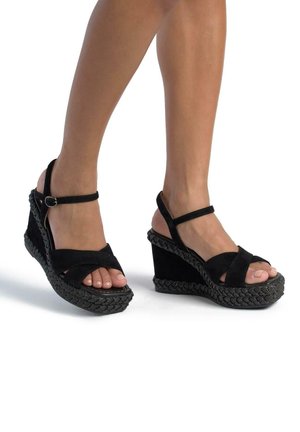 I sandali con zeppa neri in suede presentano una suola intrecciata, un design aperto sulla punta e una cinghia alla caviglia regolabile. Il tacco a zeppa offre elevazione e supporto.