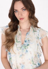 Bluse mit floralem Muster aus leichtem, transparentem Stoff und Volantärmeln. Sie hat ein blau-grünes Blumenmuster, einen Bindekragen und Perlenakzente.