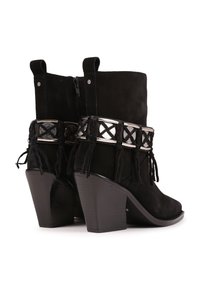 Botines de ante negro con tacón alto, que presentan una banda decorativa de plata y acentos de flecos. Cremallera trasera y tiradores para facilitar el uso.
