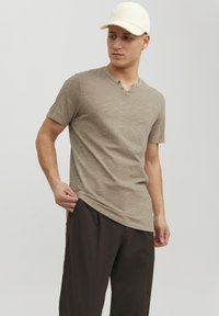 Kortærmet, olivengrøn V-hals t-shirt med to knapper, parret med mørke bukser. Blød tekstur og letvægts stof. Standard pasform.