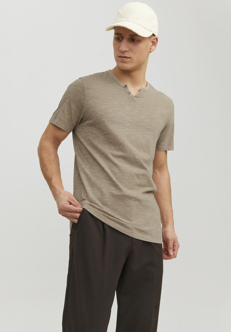 Kortærmet, olivengrøn V-hals t-shirt med to knapper, parret med mørke bukser. Blød tekstur og letvægts stof. Standard pasform.