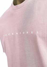 Helles rosa Baumwoll-T-Shirt mit Rundhalsausschnitt und dem Text "JACK & JONES" in Weiß, zentriert auf der Vorderseite. Glatte Textur, lässiges Design.