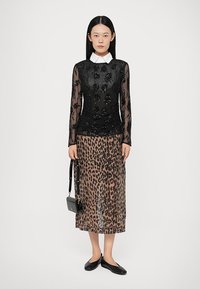 Haut noir à manches longues avec des perles florales, associé à une jupe midi à imprimé léopard. Le modèle porte des ballerines noires et tient un petit sac à main.