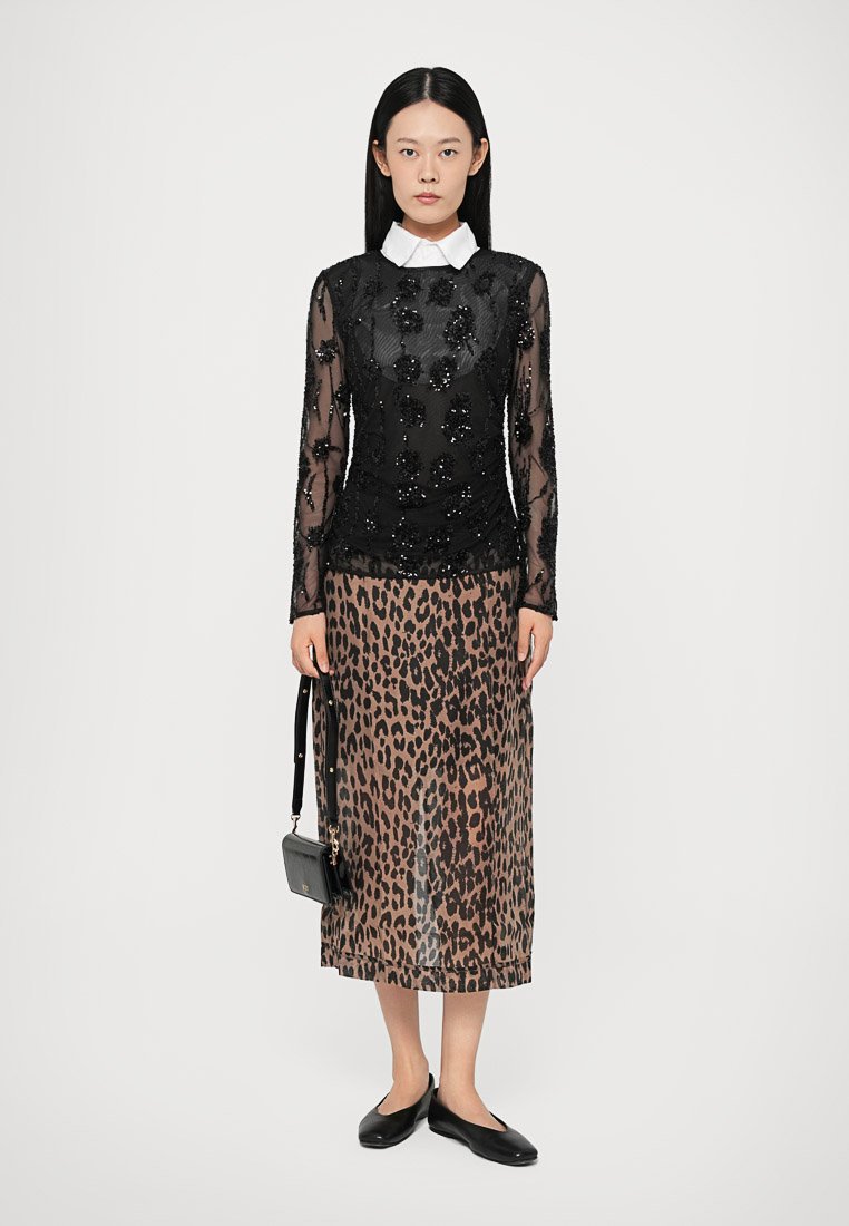 Haut noir à manches longues avec des perles florales, associé à une jupe midi à imprimé léopard. Le modèle porte des ballerines noires et tient un petit sac à main.