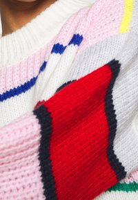 Pull en maille à rayures horizontales blanc, rose, bleu et rouge. Présente un col côtelé confortable et une surface texturée. Accents géométriques colorés.