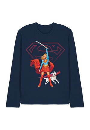 Supergirl in blue and red costume holding a sword aloft, standing next to a white dog, with a large red Superman logo behind her on navy shirt.