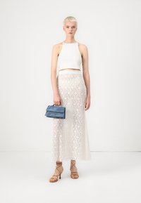 Biely skrátený tank top, čipkovaná biela maxi sukňa s kvetinovým vzorom, holé sandále na opätku a malá modrá kabelka. Hladká textúra.