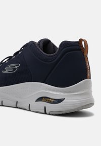 Zapato navy con parte superior de malla, entresuela blanca y detalle texturizado en el talón. Presenta la marca 'ArchFit' cerca de la suela para soporte del arco.