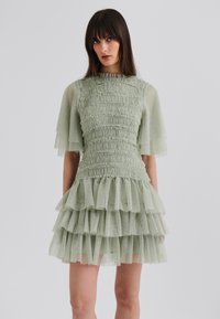 Light green dress featuring a textured, smocked bodice, short ruffled sleeves, and a tiered ruffled skirt for added volume and detail.