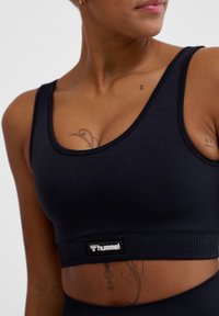 Zwarte sportbeha van gestructureerde stof, met een brede elastische band met een logotag, die een comfortabele pasvorm en een eenvoudig ontwerp biedt.