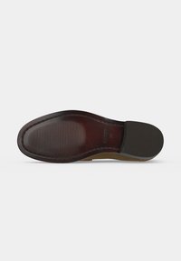 Semelle d’une chaussure de ville en cuir marron avec l’avant rainuré et talon en caoutchouc pour l’adhérence, indiquant la taille 39 et embossage de la marque.