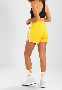 Yellow athletic shorts with white side stripes, elastic waistband, and a relaxed fit. Paired with white sneakers and striped socks.