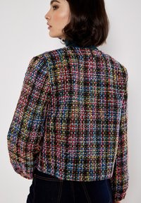Giacca in tweed colorata caratterizzata da un motivo a quadri con fili neri, rossi, blu e gialli. Design accorciato con maniche lunghe.