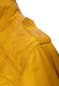 Gelbe Lederjacke mit strukturiertem Finish, ausgeprägten Schulternähten und detaillierten Nähten entlang des Kragens und der Schultern.