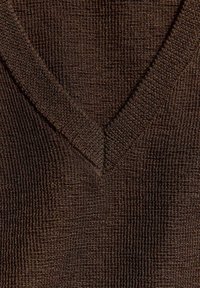 Gros plan d’un tissu tricoté brun foncé montrant un décolleté en V texturé avec des bords côtes.