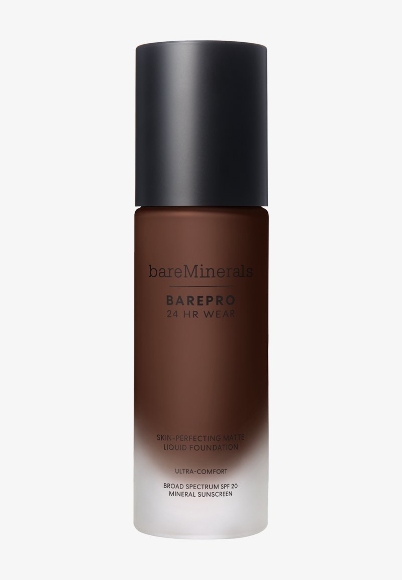 Bruine glazen fles met een zwarte matte dop. Etiket vermeldt "bareMinerals" en "BAREPRO 24 HR WEAR" met witte tekst. Vloeibare foundation binnenin, halfdoorzichtig.