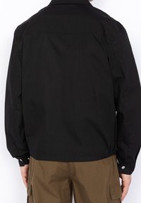 Black jacket with a simple design, featuring a collar and elasticated waist. Made of smooth fabric, it has snap button accents at the cuffs.