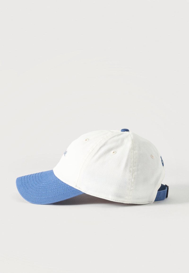 Weißes Baseballcap mit blauem, gebogenem Schirm und verstellbarem hinterem Riemen, seitlich auf hellem Hintergrund dargestellt.
